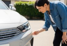 Comment lire les exclusions de garantie de son contrat auto Automobiliste inspectant une petite rayure sur le pare-chocs de sa voiture avant de contacter son assureur