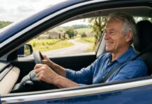 Assurance auto tous risques senior : ce qui change après 70 ans Conducteur senior souriant conduisant sa voiture sur une route de campagne en France