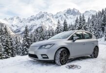 Pneus hiver et loi Montagne : ce que votre assurance auto couvre en cas d’accident Voiture avec pneus hiver sur une route enneigée de montagne, chaînes à neige posées à côté de la roue