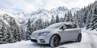 Pneus hiver et loi Montagne : ce que votre assurance auto couvre en cas d’accident Voiture avec pneus hiver sur une route enneigée de montagne, chaînes à neige posées à côté de la roue