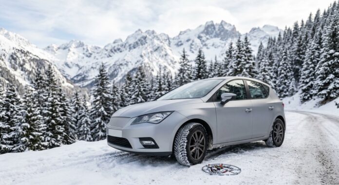 Voiture avec pneus hiver sur une route enneigée de montagne, chaînes à neige posées à côté de la roue
